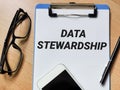 Phrase DATA STEWARDSHIP written on paper clipboard with pen,smartphone and eye glasses.