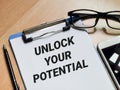 Phrase UNLOCK YOUR POTENTIAL written on paper clipboard with pen,smartphone and eye glasses.