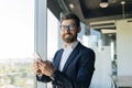 Business and telecommuting concept. Portrait of happy middle aged man using smartphone, texting with client in office Royalty Free Stock Photo