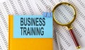 BUSINESS TRAINING text on sticker on notebook with magnifier and chart. Business