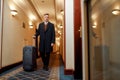 Business travel. Middle-aged businessman in coat with suitcase walking along the hall, while looking for his room in a Royalty Free Stock Photo