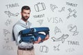 Business trip. Excited and handsome man is holding his suitcase and looking at camera while standing against grey Royalty Free Stock Photo