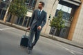 Business trip. Full length of young and handsome bearded man in suit pulling his luggage and looking away while walking Royalty Free Stock Photo