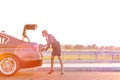 Mature businesswoman removing suitcase from car trunk on road against sky