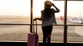 Business trip of young woman in hat which holding the luggage and looking the airplane in the hall room with sunlight in the