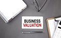 BUSINESS VALUATION Text written on the card with notebook and clipboard, grey background Royalty Free Stock Photo