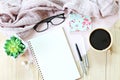 Flat lay or top view of knitted scarf, open blank notebook paper, coffee cup and eyeglasses on wooden background