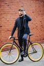 Business on wheels. Stylish confident businessman ride with his bicycle at building brick wall