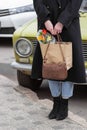 Business woman in black vintage coat holding retro leather handbag and shopping bag with flowers. Retro car background. Royalty Free Stock Photo