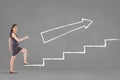 Business woman climbing stairs against grey background with white arrow