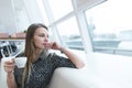 A business woman with a cup of coffee in her hands sits in a modern, light restaurant and looks out the window.