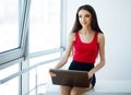 Business. Business Woman Dressed in Red T-Shirt and Black Skirt is Working on the Computer. Girl Sits on the Table and Royalty Free Stock Photo