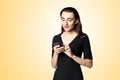 Business woman fatal woman in a black dress with red lipstick looks at her phone, isolated on a yellow background Royalty Free Stock Photo