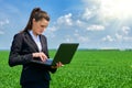 Business woman in green grass field outdoor work on laptop. Young girl dressed in black suit. Beautiful spring landscape with clou Royalty Free Stock Photo