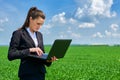 Business woman in green grass field outdoor work on laptop. Young girl dressed in black suit. Beautiful spring landscape with clou Royalty Free Stock Photo