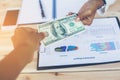 Business woman gripping The United States hundred-dollar bills in her hand and some put on the table full with business charts and Royalty Free Stock Photo