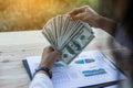 Business woman gripping The United States hundred-dollar bills in her hand and some put on the table full with business charts and Royalty Free Stock Photo