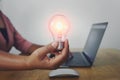 business woman hand holding light bulb with using laptop in office. concept saving energy power