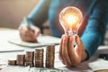 business woman hand holding lightbulb with coins stack on desk. concept saving energy Royalty Free Stock Photo