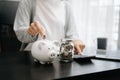 Business woman hand putting money coin into piggy bank with step of growing stack coins for saving money at modern office Royalty Free Stock Photo