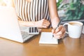 Business woman hand working at a computer and writing on a noteped with a pen.