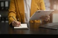 Business woman hand working at laptop and writing on a notepad with a pen in the office. on the wooden desk Royalty Free Stock Photo