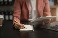 Business woman hand working at laptop and writing on a notepad with a pen in the office. on the wooden desk Royalty Free Stock Photo