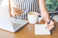 Business woman hand is writing a pen notebook and using a phone Royalty Free Stock Photo