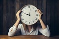 Business woman hides face behind clock, symbolic of time pressure