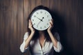 Business woman hides face behind clock, symbolic of time pressure