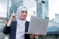 Business woman in hijab and suit is using a laptop and holding her index finger up outdoors. Royalty Free Stock Photo