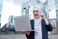 Business woman in hijab and suit is using a laptop and holding her index finger up outdoors. Royalty Free Stock Photo