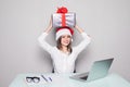 Young business woman holding gift box over head while working on desk office concept office christmas and happy new year. Royalty Free Stock Photo