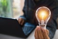 Business woman holding light bulb on the desk in office and using computer in financial,accounting,energy,idea concept. Royalty Free Stock Photo