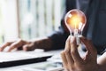 Business woman holding light bulb on the desk in office and using computer in financial,accounting,energy,idea concept