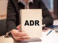 Business woman holds a notebook with the text ADR. Abbreviation ADR