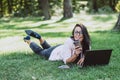Business woman, lies in a summer grass park, using a laptop with a glass of coffee in hand. Remote work during quarantine. Woman Royalty Free Stock Photo