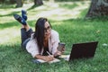 Business woman, lies in a summer grass park, using a laptop with a glass of coffee in hand. Remote work during quarantine. Woman Royalty Free Stock Photo