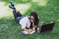 Business woman, lies in a summer grass park, using a laptop. Remote work during quarantine. Woman with coffee. Outdoors. Soft Royalty Free Stock Photo