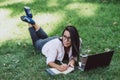 Business woman, lies in a summer grass park, using a laptop. Remote work during quarantine. Woman with coffee. Outdoors. Soft Royalty Free Stock Photo