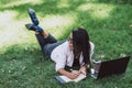 Business woman, lies in a summer grass park, using a laptop. Remote work during quarantine. Woman with coffee. Outdoors. Soft Royalty Free Stock Photo