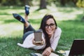 Business woman, lies in a summer grass park, using a laptop smiles and holds out a glass with coffee. Remote work during Royalty Free Stock Photo