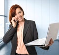 Business woman with red hair at work smiling with laptop computer talking busy on mobile phone Royalty Free Stock Photo