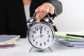 Business woman`s hand reaches out to touch alarm clock to stop time while sitting at her office desk. Selective focus of alarm Royalty Free Stock Photo