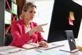 Business woman with serious face at office desk points her finger at computer screen.