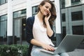 Business woman sits in urban park and typing text on modern laptop and talk by mobile phone Royalty Free Stock Photo