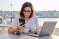 Business woman sitting in outdoor cafe with cup of coffee using laptop and smart phone Royalty Free Stock Photo