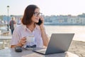 Business woman sitting in outdoor cafe with cup of coffee using laptop and smart phone Royalty Free Stock Photo