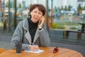 A business woman is sitting at a table in a summer cafe. The woman is talking on the phone and writes in a notebook Royalty Free Stock Photo