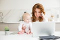 Business woman sitting at the table working on laptop while holding her joyful little baby near Royalty Free Stock Photo